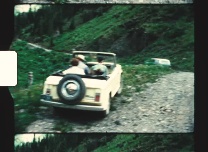 Lightcolored convertible stopped on a mountain road with three people on board