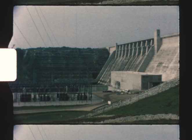 A dam under construction with powerlines stretching across the scene at midday