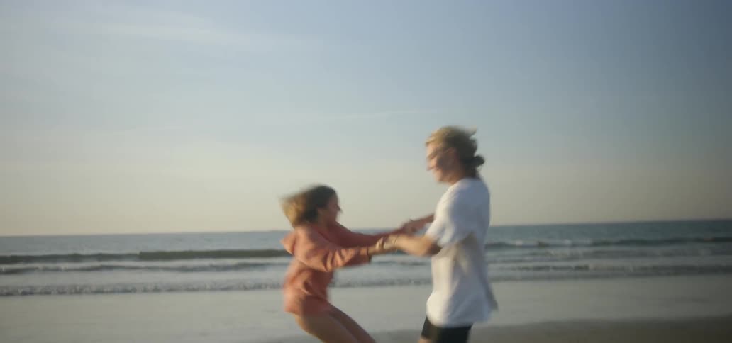 Man and woman holding hands and spinning around on beach