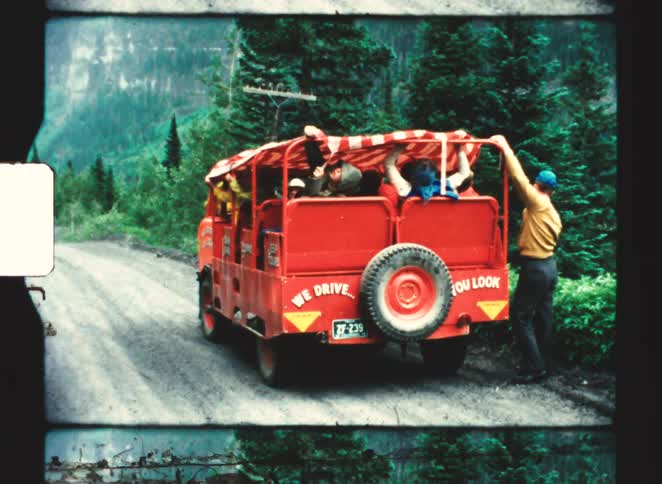 Red tour vehicle traveling on a treelined road with passengers adjusting the canopy