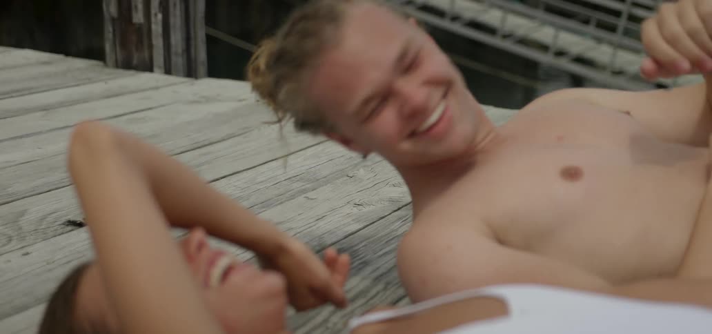 A couple on a dock shield their eyes from the sun while laughing