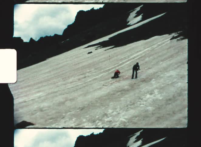 People in winter clothing walk along steep slope with snow and exposed rocks