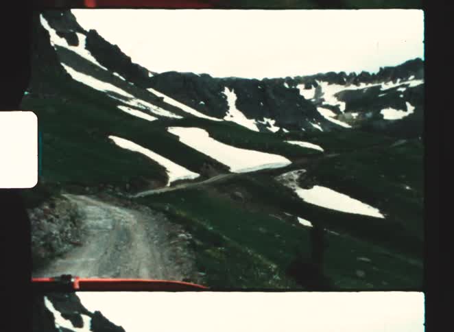Dirt road winding through a mountainous valley with patches of snow on the slopes