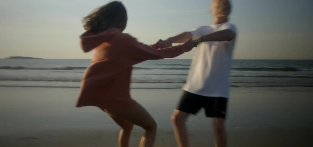 A man and woman hold hands and spin on a beach