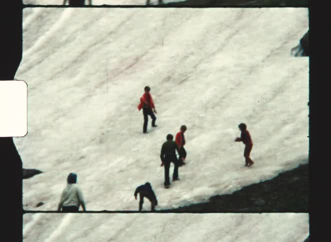 Group of people walking and crouching on a snowfield in a mountainous area