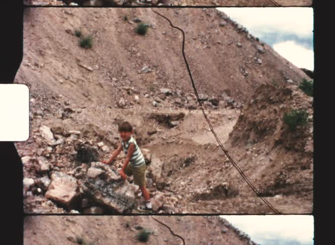 Child standing beside rock in barren terrain with steep slopes