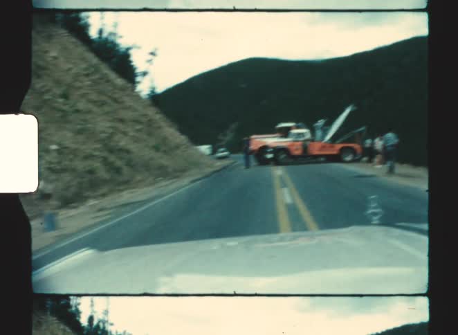 An orange tow truck blocks the doublelaned mountain highway while personnel work around it near a steep rocky slope