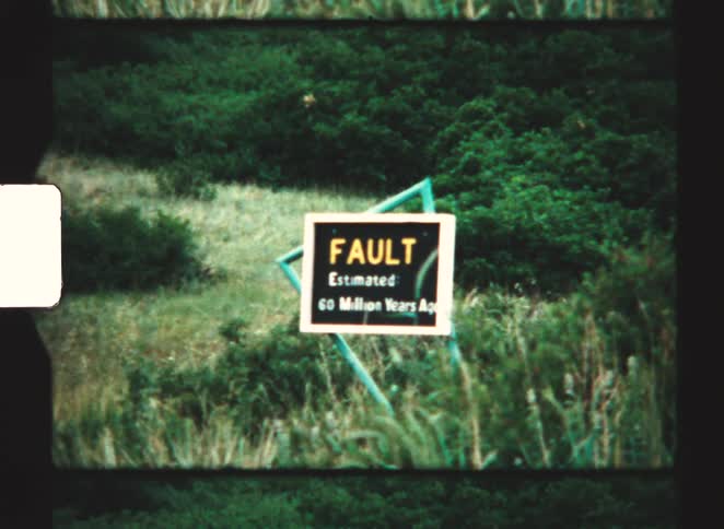 A grainy archival film clip shows a sign marking a geological fault estimated to be 60 million years old surrounded by overgrown green brush