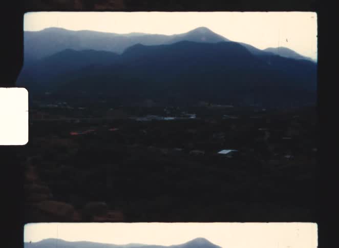 Dark mountains stand out against lit sky at dusk with visible structures in the valley