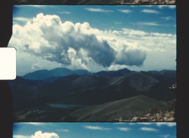 Man stands looking at mountains and the river winding amongst them on a cloudy day
