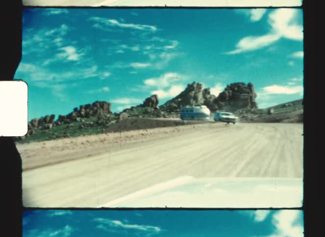 pikes peak colorado A white car and a vintage blue rv are moving in opposite directions on a dusty road through a rocky landscape under a blue sky