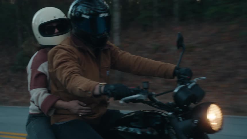 Man riding a motorcycle with his passenger holding on as they travel on a road
