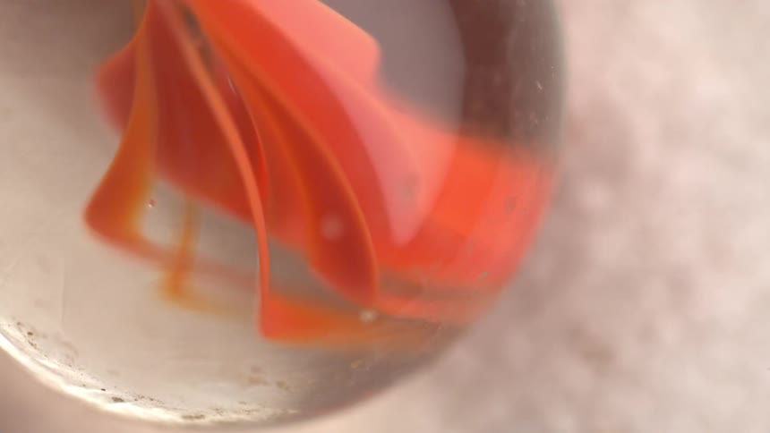 Marble in closeup displays orange internal bands on a light granular surface