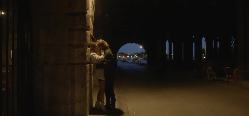 A man and woman make out while leaning against a building
