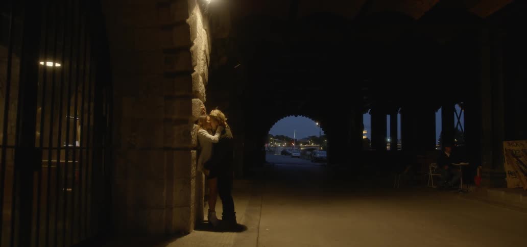A man and woman kiss in an alley