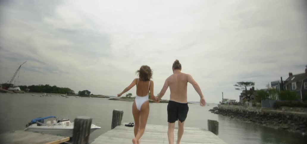 Man and woman run down a dock and jump into lake