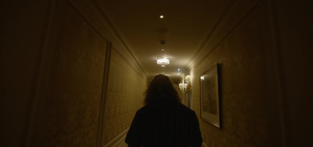 A man walks down the dark hall brushing his hair once