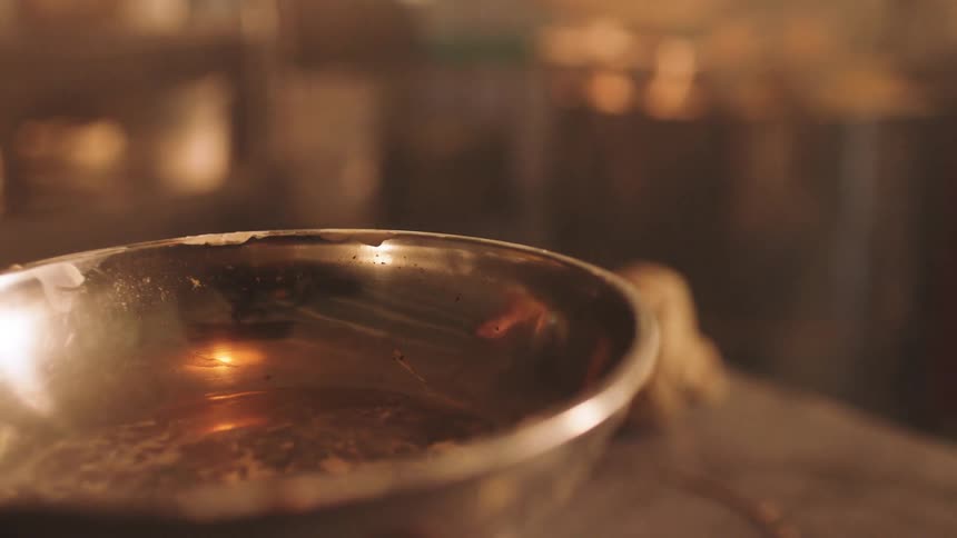The reflective interior of a stainless steel mixing bowl holding residual liquid and small bits set against a blurry warmlit background