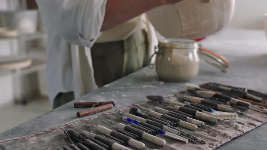 A table with several paintbrushes on an old cloth and a person putting something into a glass container