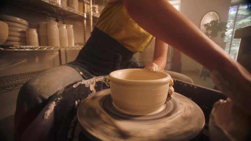 Young adult woman sitting and molding clay on a wheel indoors during day time