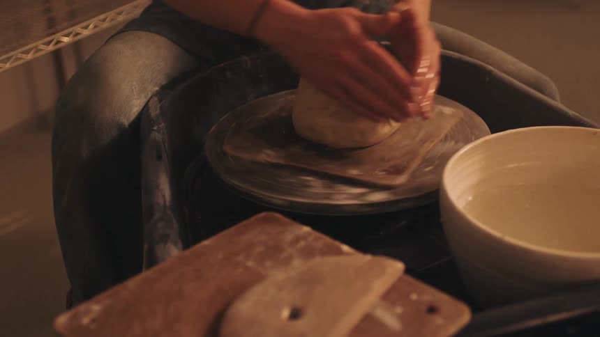 A person is sitting and rotating a piece of clay on a round surface