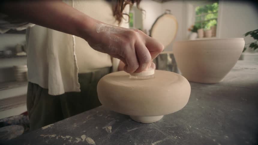 Woman stands at a table making pottery