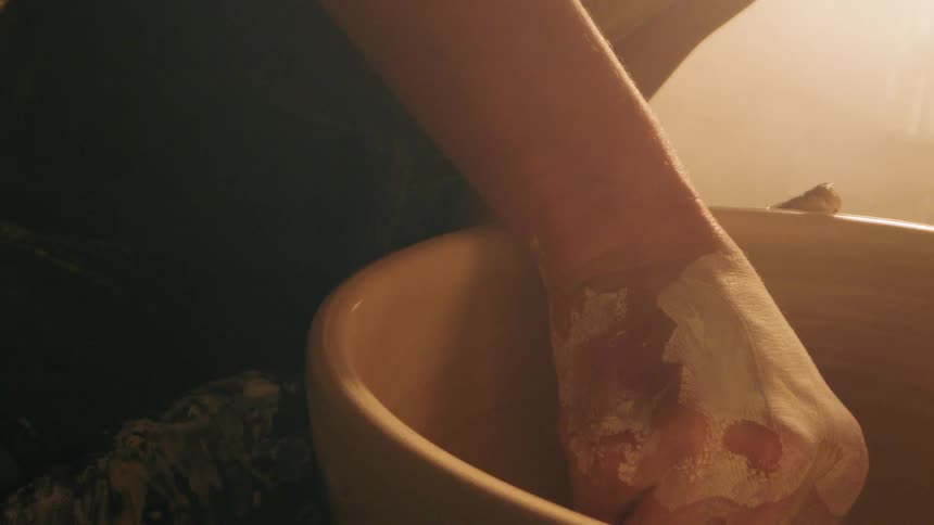 Female potter shapes a bowl turning on her pottery wheel in her workshop