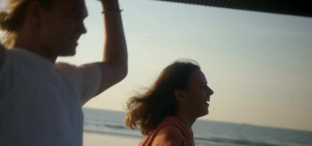 A man is carrying a surfboard on his head while walking with a woman