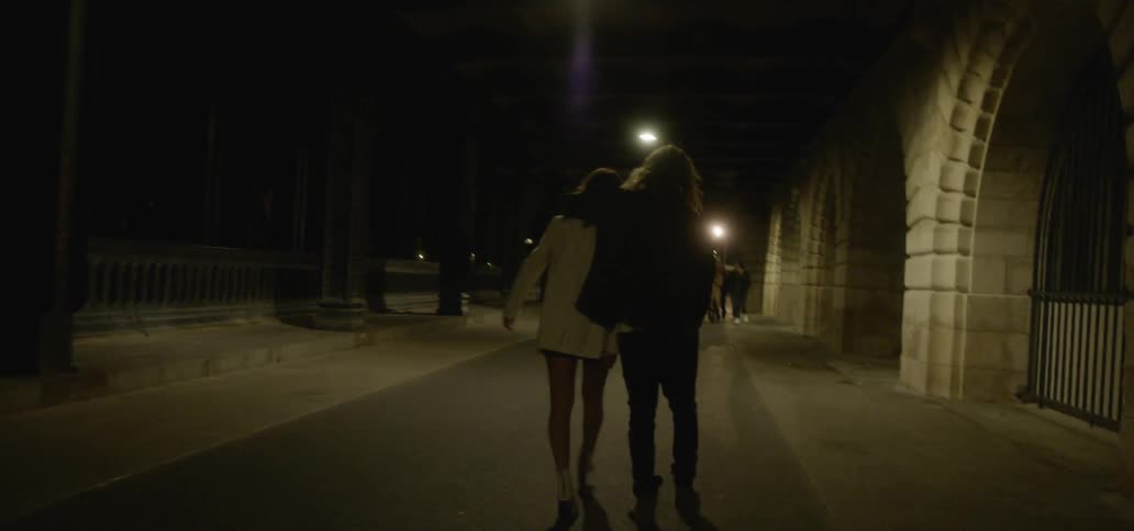 Two people walk outside of a building on a path at night