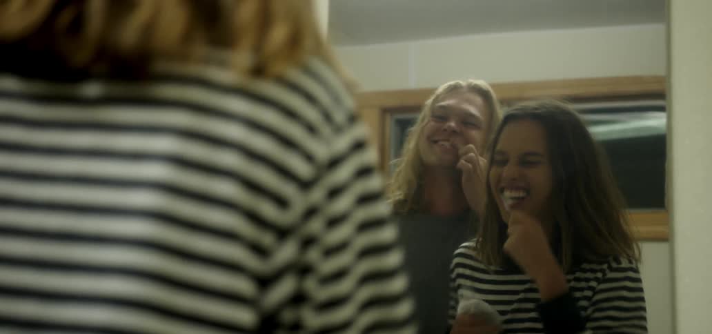 A man and woman laugh while brushing their teeth