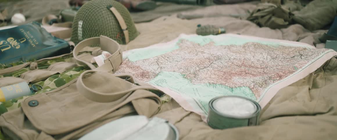 Map and hiking equipment spread out on a blanket with a military helmet and hand grenade