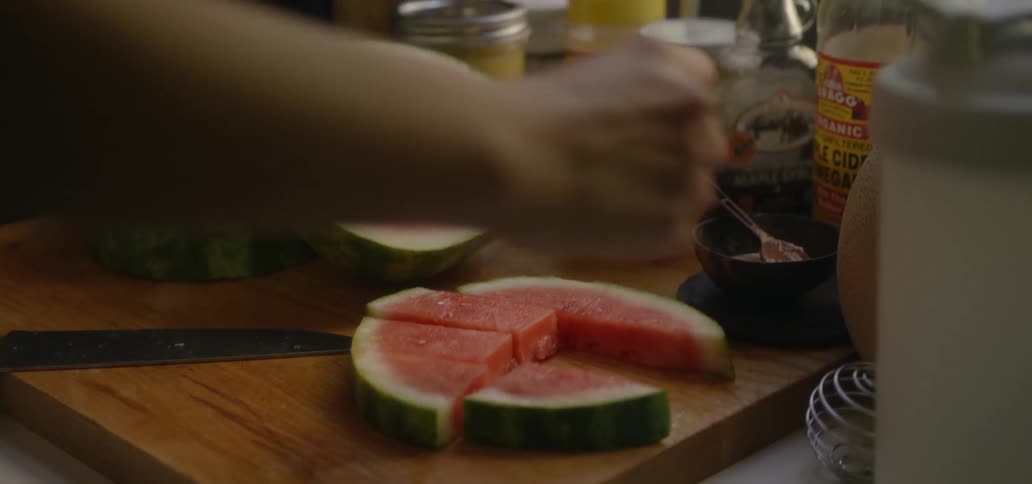 A person taking pieces of watermelon off a cutting board