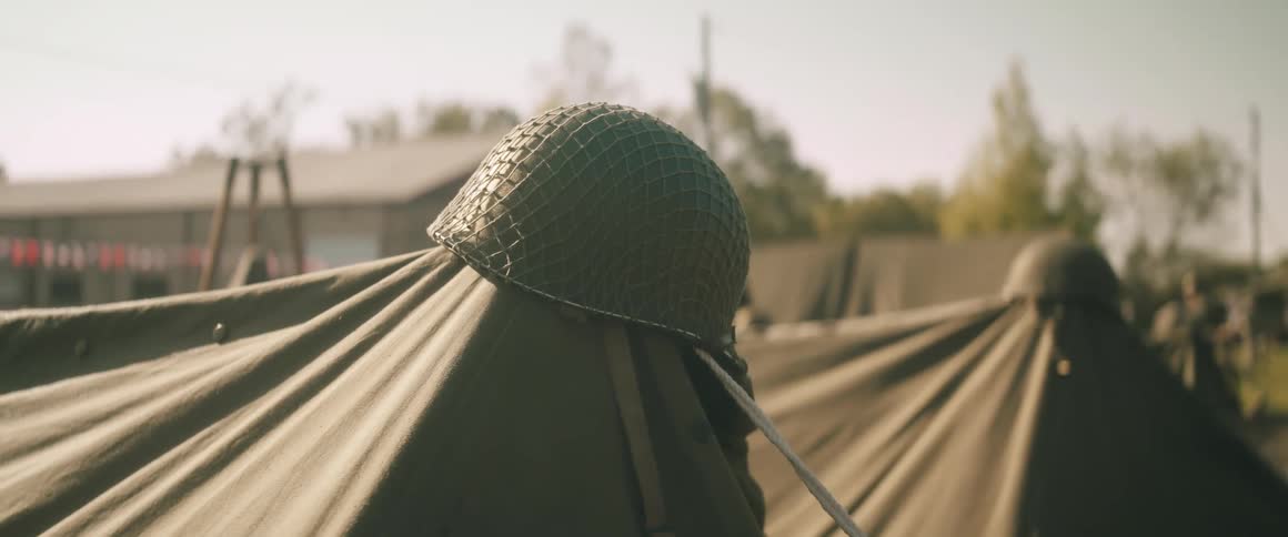 Military helmet with netting resting on tent in temporary encampment