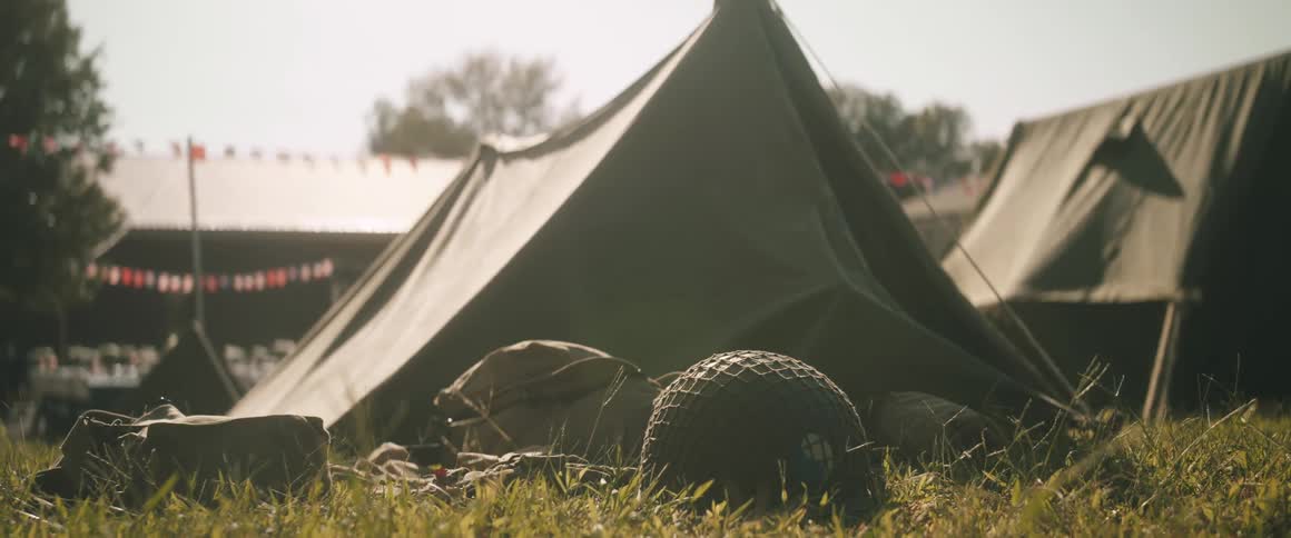 An army helmet in front of a green tent on the grass