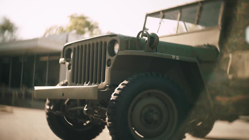 A lowangle closeup reveals the rugged front grille and heavy tread tire of a vintage military jeep parked on a sunny street bathed in warm natural light