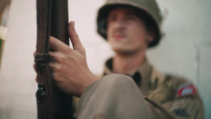 Military hand gripping rifle with uniform and helmet in focus