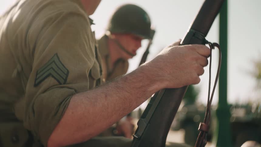 Two military personnel holding their weapons wearing full uniforms and helmets rising from a squatting position after examining a situation at midday