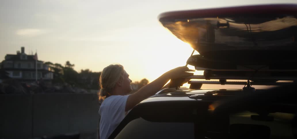 A man is tying a surfboard to the top of his vehicle