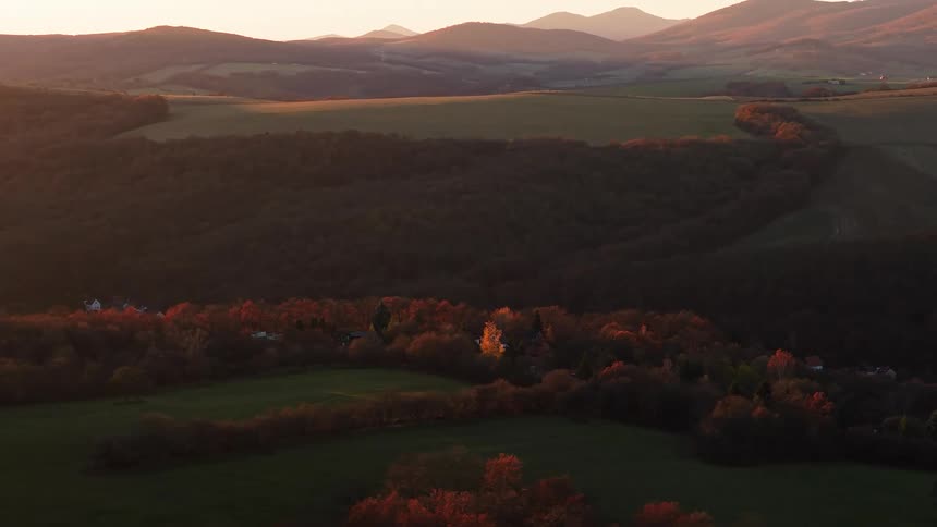 Woods surround a town standing among hills under a red sky on an autumn day