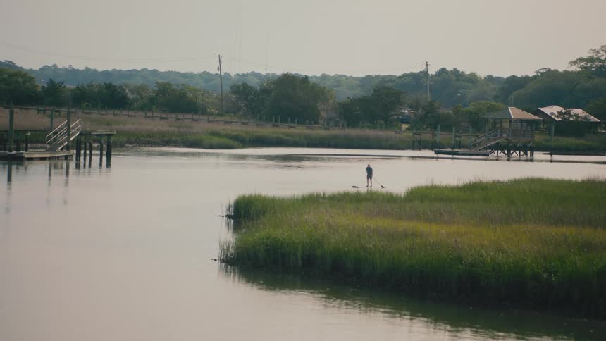 Man standing on a paddle board paddles while rounding the riverbank on a river on a foggy day