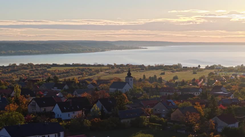 A suburban area with buildings surrounded by autumn trees with an ocean view visible in the background