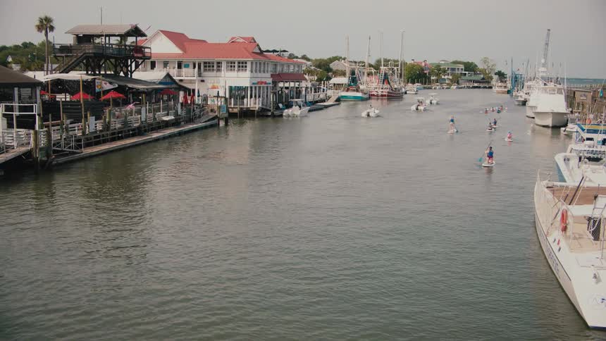 View of the harbor with anchored boats and several people practicing standup paddle in the channel
