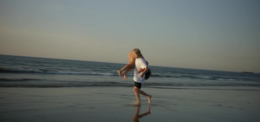 A man lifts a woman over his shoulder on a sandy beach