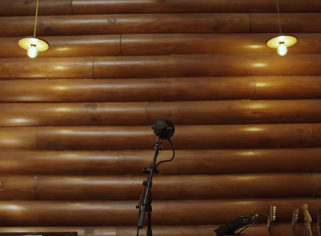 Microphone on stand in front of log wall with hanging lights and musical instruments nearby