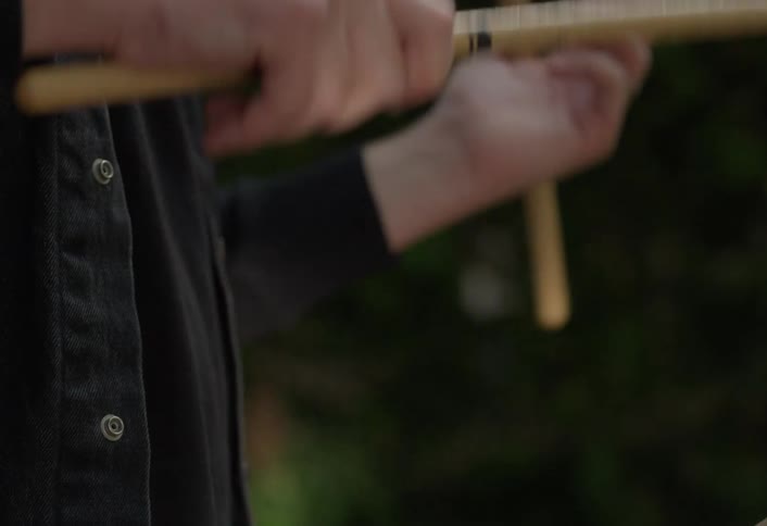 A closeup of a persons hands wearing a dark shirt holding and twirling two wooden drumsticks in a ready position against a very dark blurred background