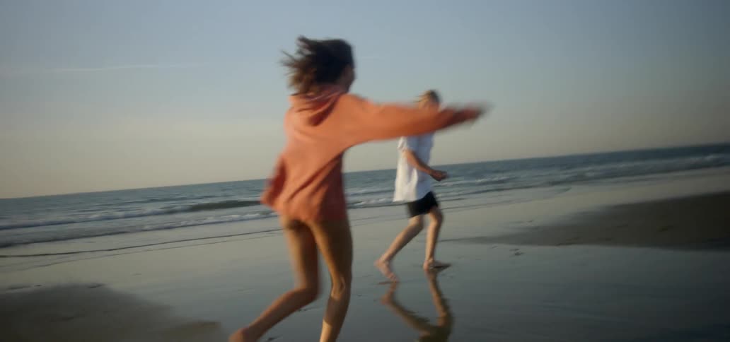 A woman does cartwheels with a man running down a beach by the water