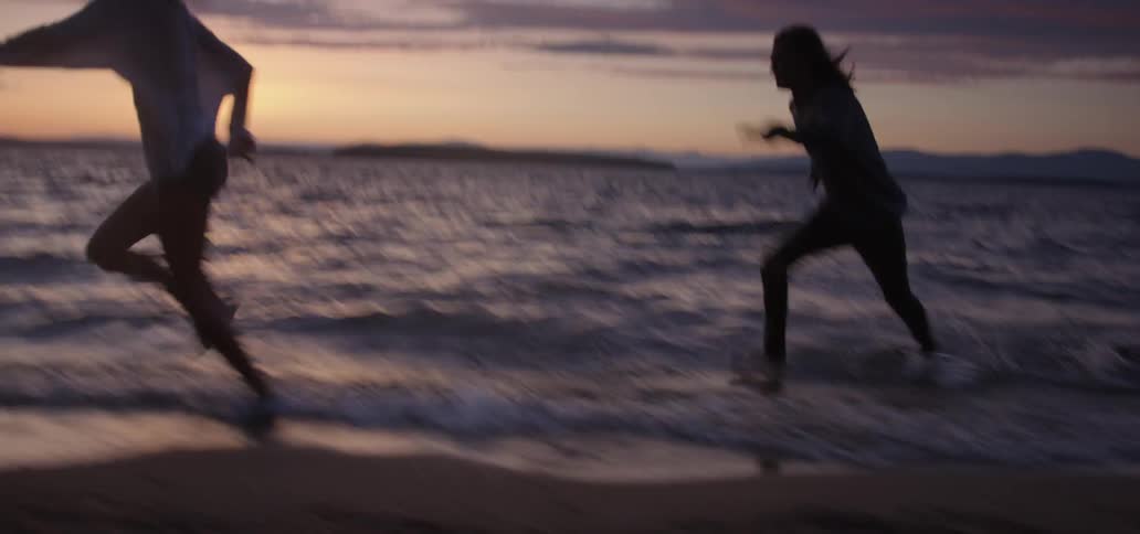 A man and woman run on the beach at sunset