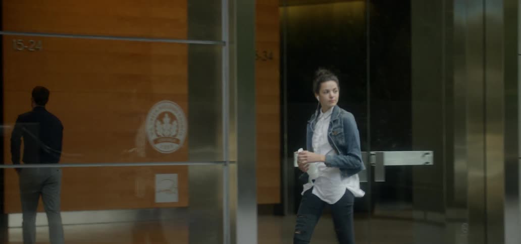 A woman walks on a city sidewalk while wearing earbuds