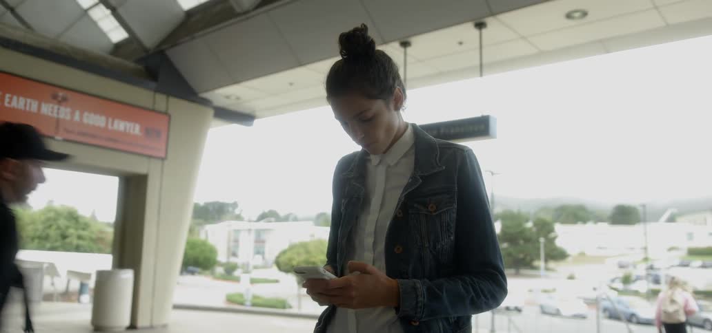 A woman checks her phone in front of a building