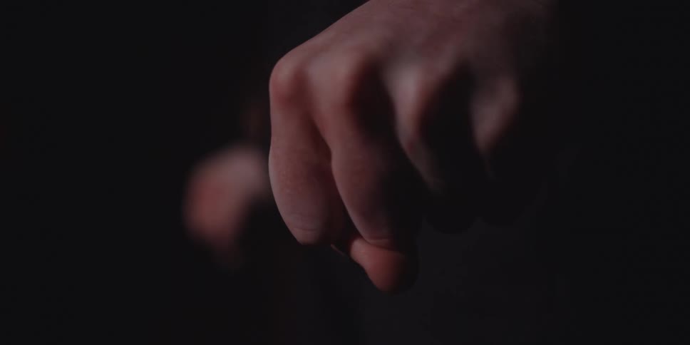 A person clenching their fist in anger while standing in a dark room